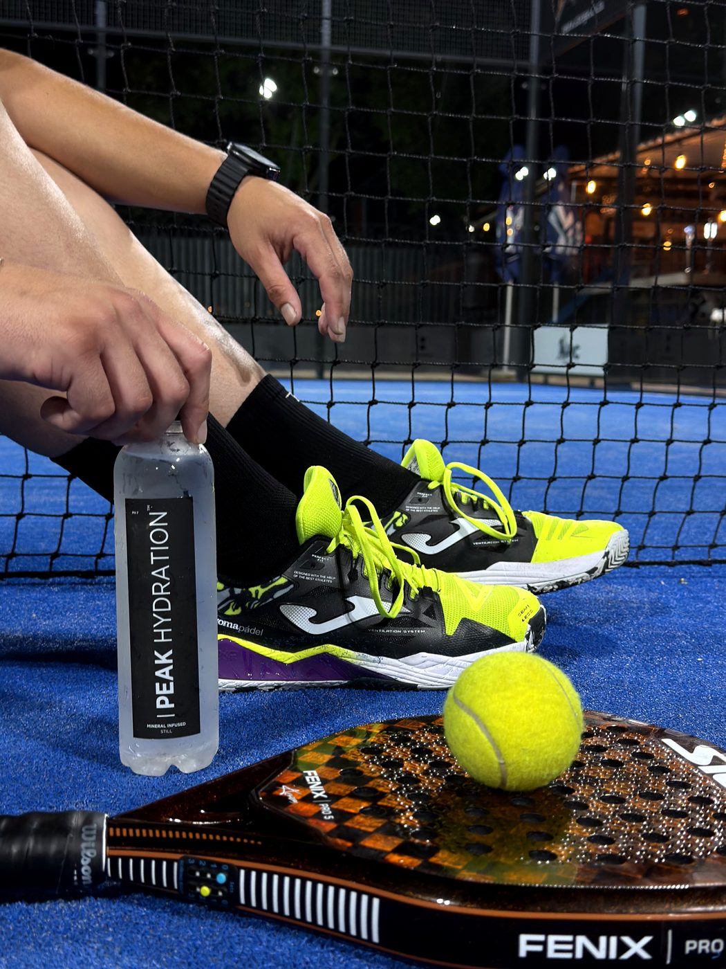 A bottle of Peak Hydration courtside, next to a padel racket and ball
