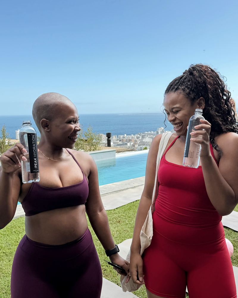 Two women with Peak Hydration by a pool above the sea